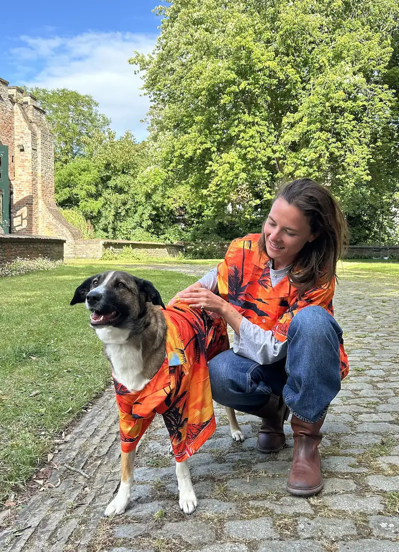 Een vrouw en een hond dragen bijpassende kleurrijke outfits in een groene omgeving.