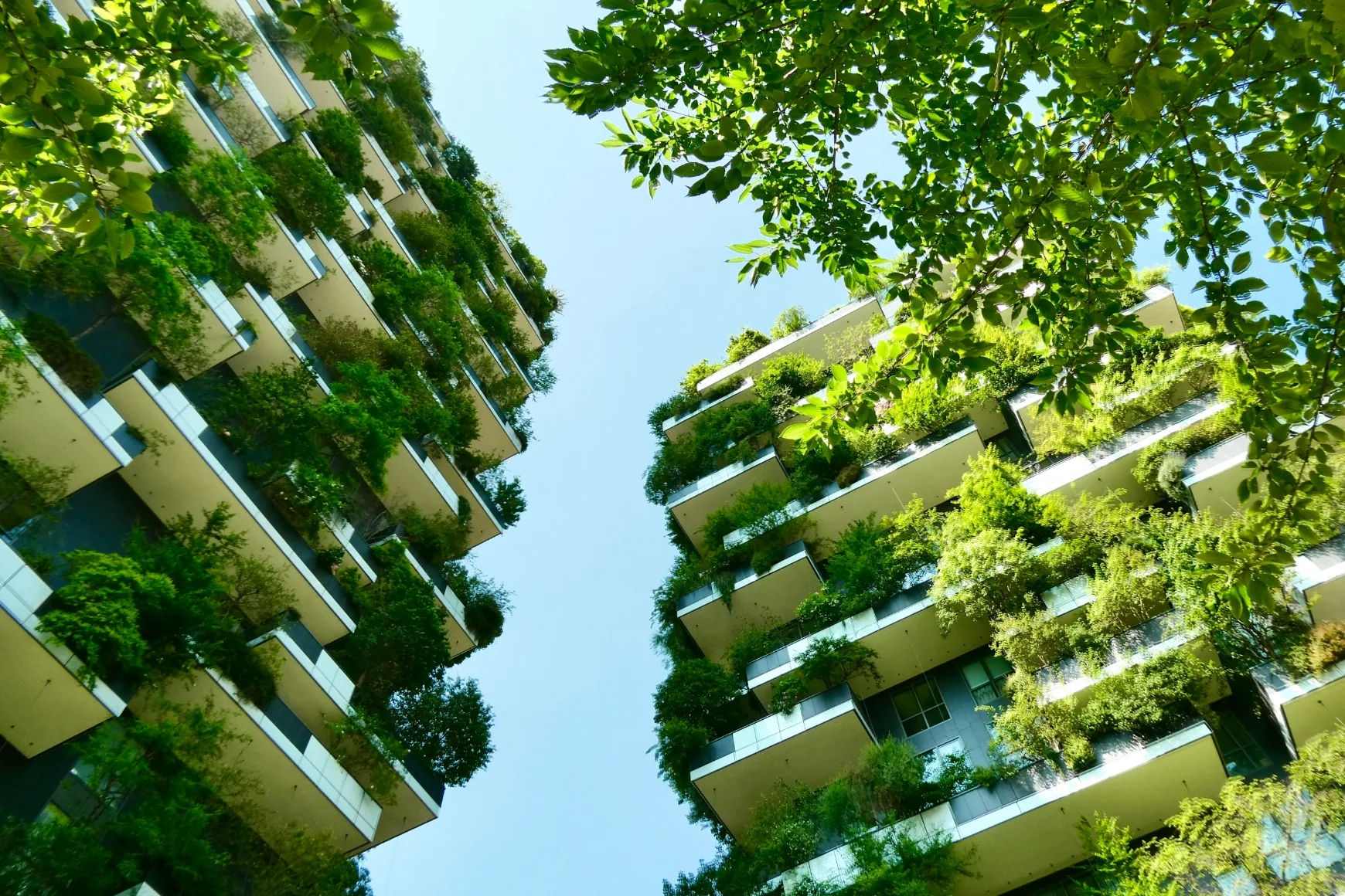 Groene woontorens met beplante balkons tegen een heldere blauwe lucht, gezien van onderaf.