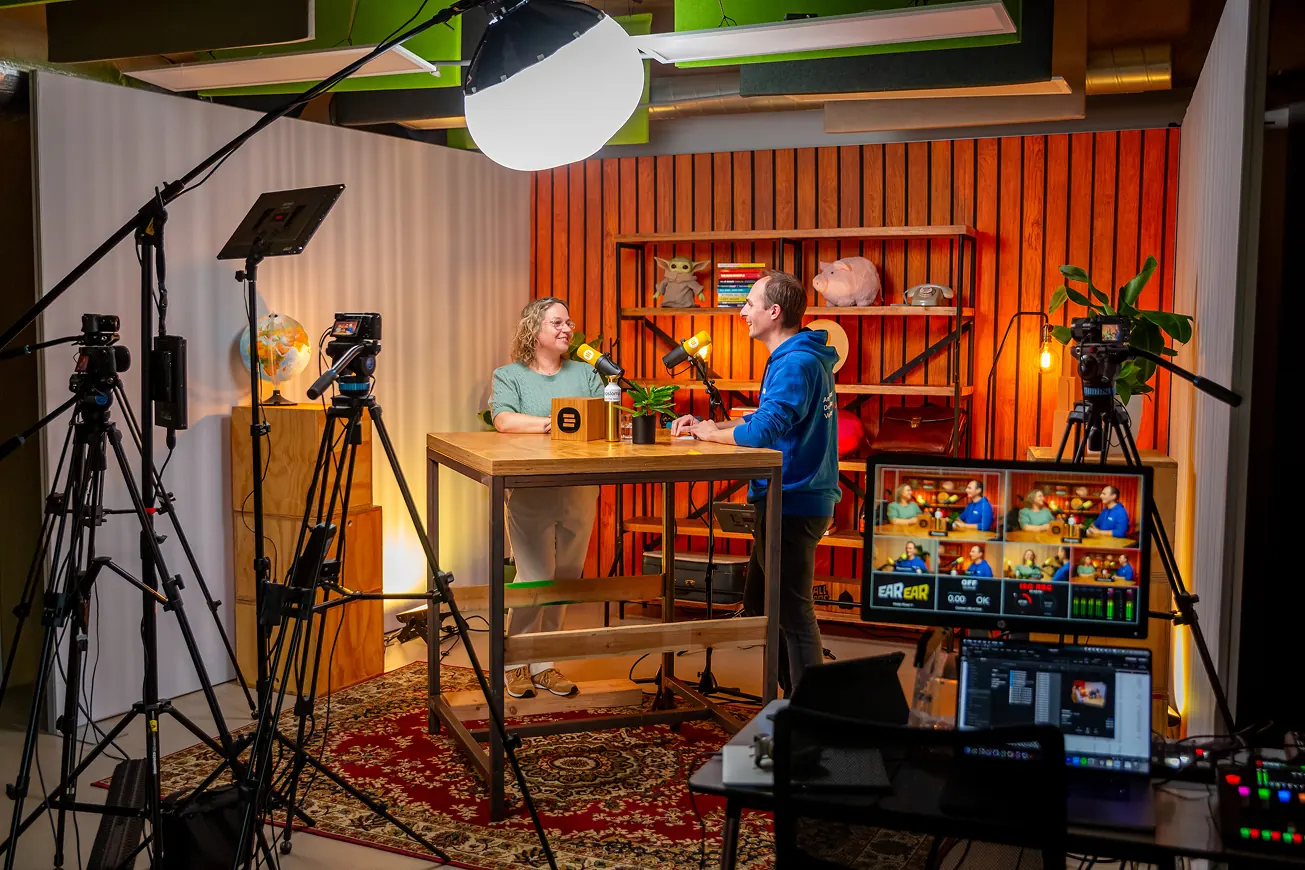 Twee mensen nemen een podcast op in een kleurrijke studio met cameraapparatuur en studiolampen.