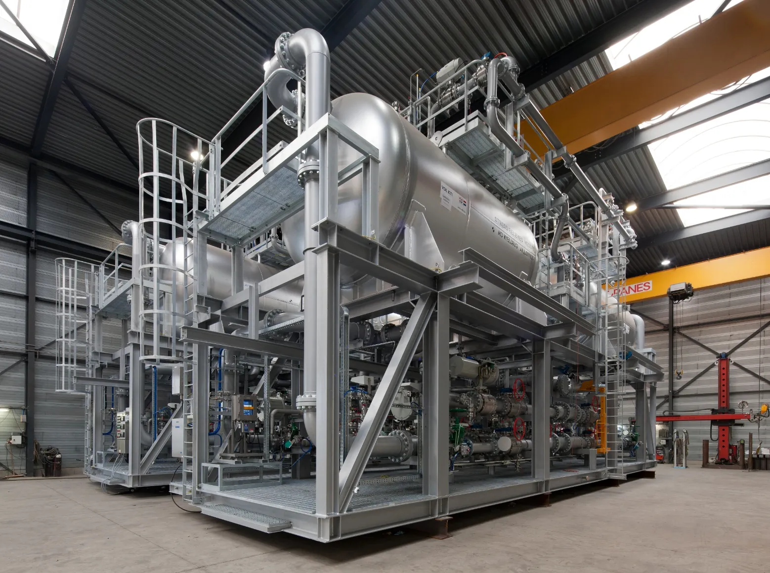 Grote industriële installatie van FB Group in een fabriekshal, bestaande uit metalen buizen, tanks en platforms.
