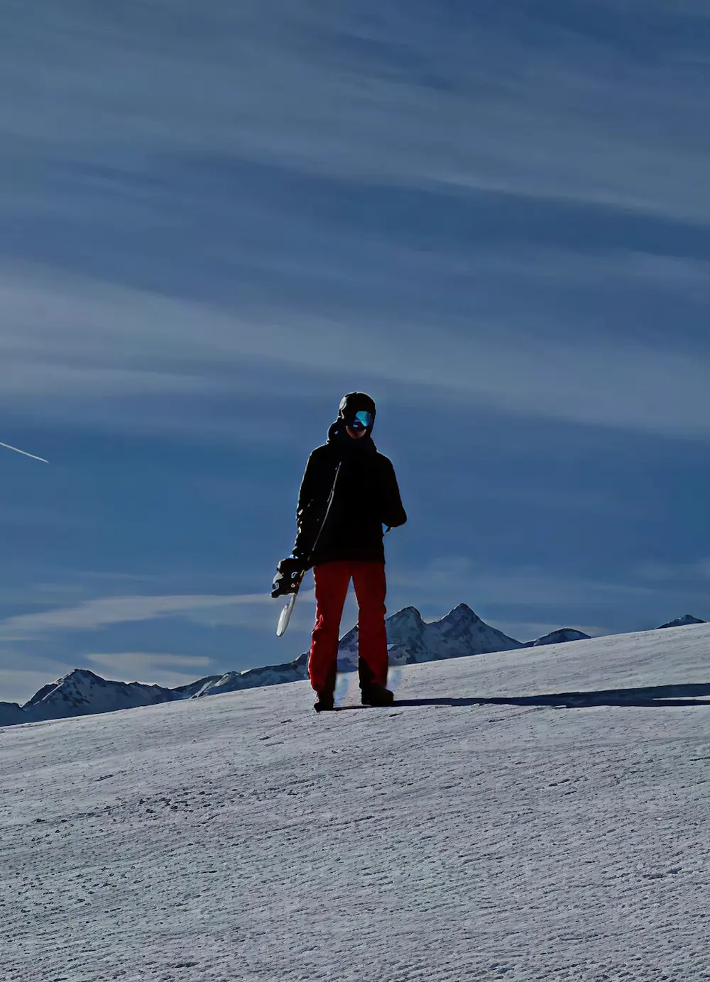 Persoon met snowboard op een besneeuwde berghelling, met een heldere blauwe lucht op de achtergrond.