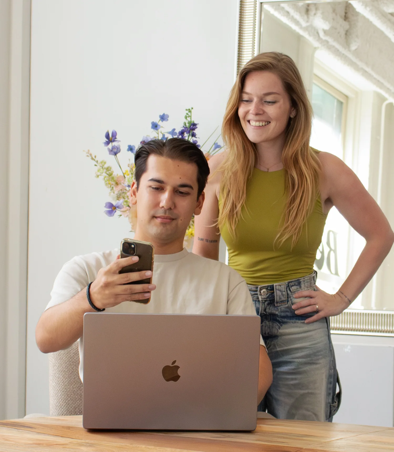Twee collega’s bekijken samen iets op een smartphone achter een laptop in een creatieve werkomgeving.