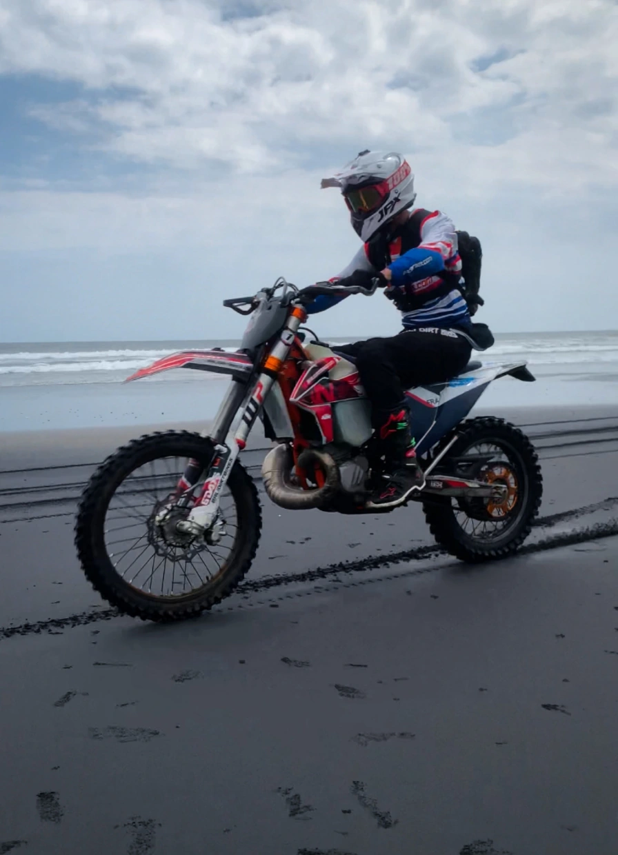 Motorrijder Sven Hover rijdt met een crossmotor over het natte zandstrand langs de zee.
