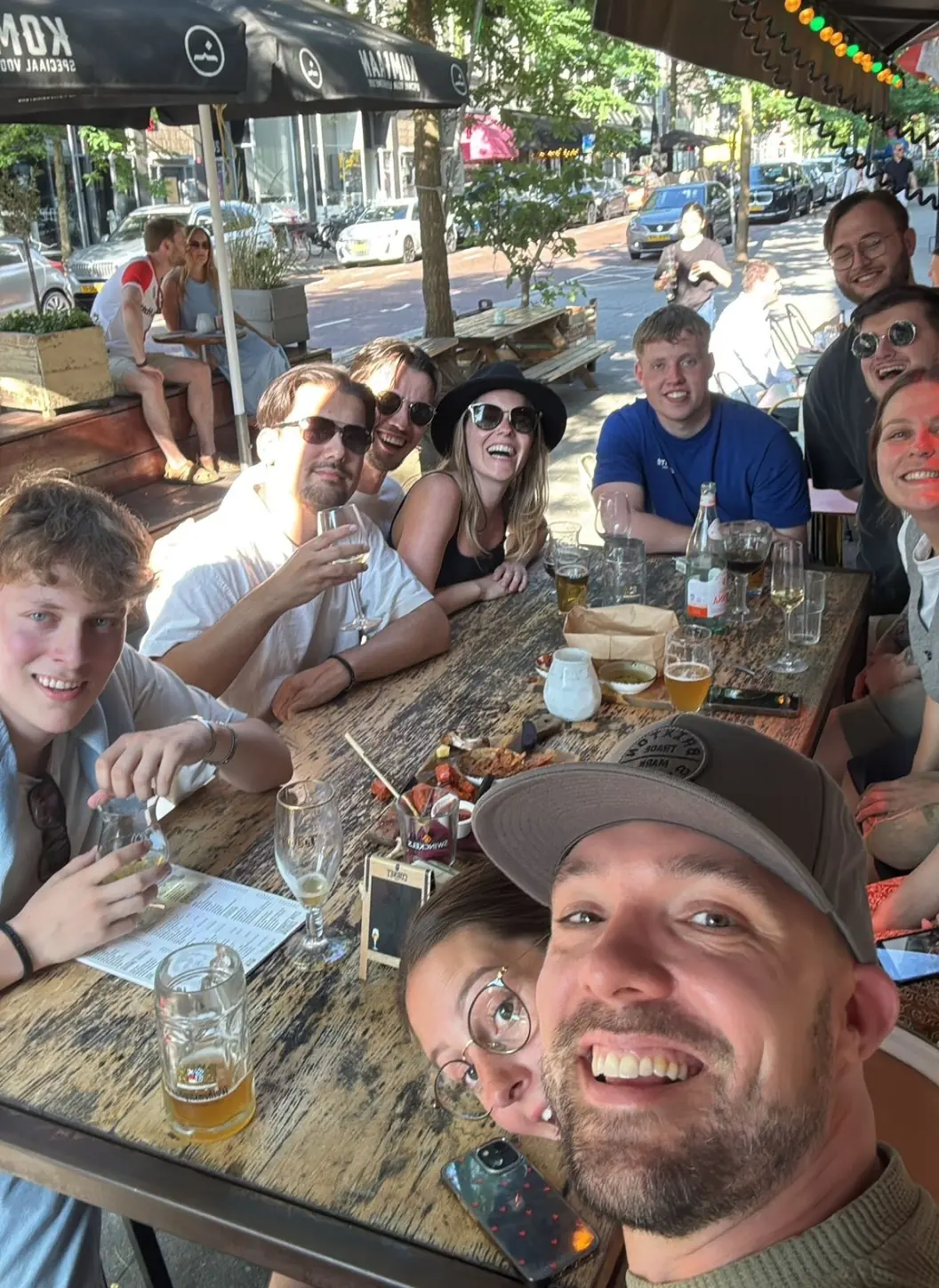Groep collega's geniet van een gezellig teamdiner op een zonnig terras.