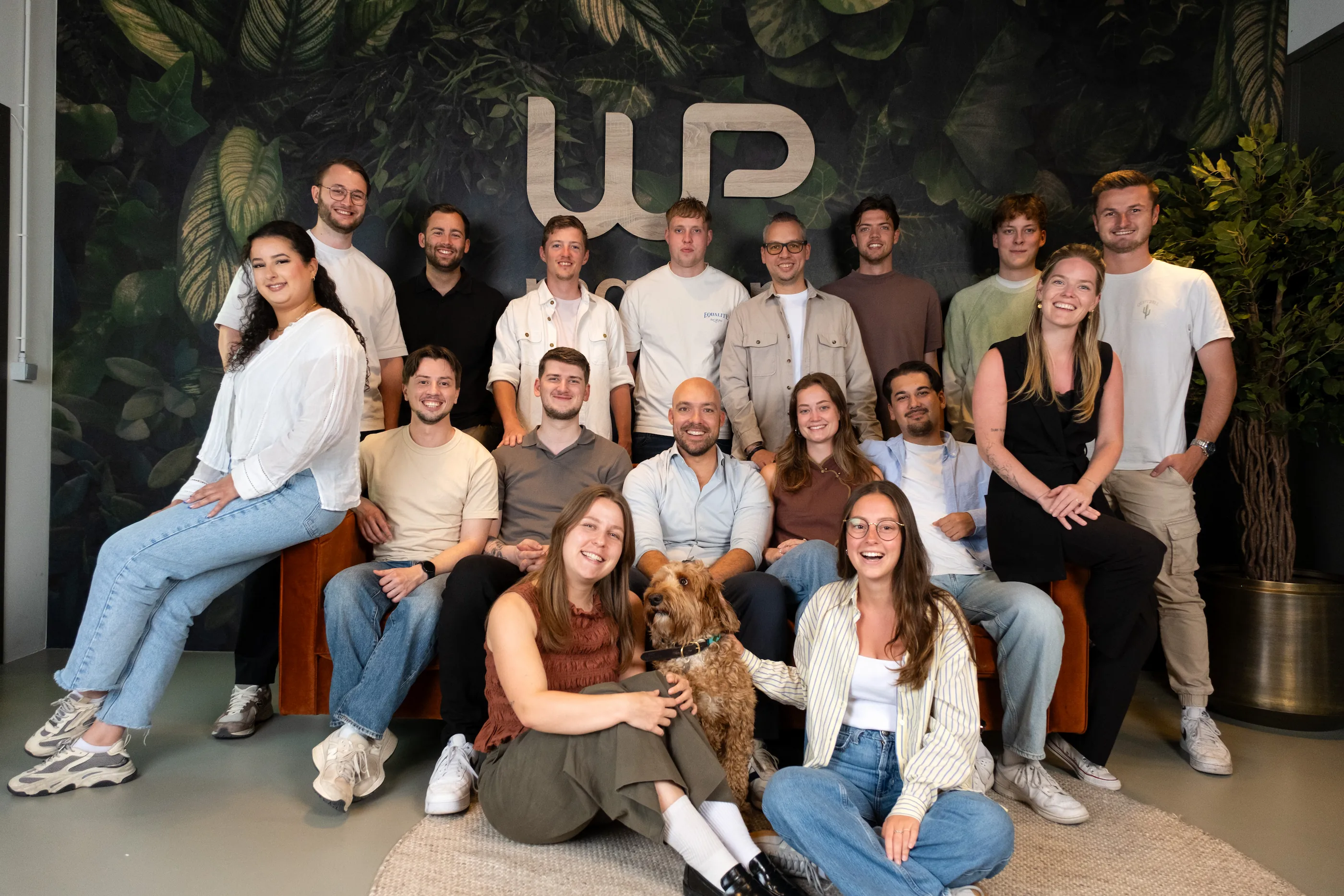 Group photo of the WP team posing together in front of a green wall with the WP logo.